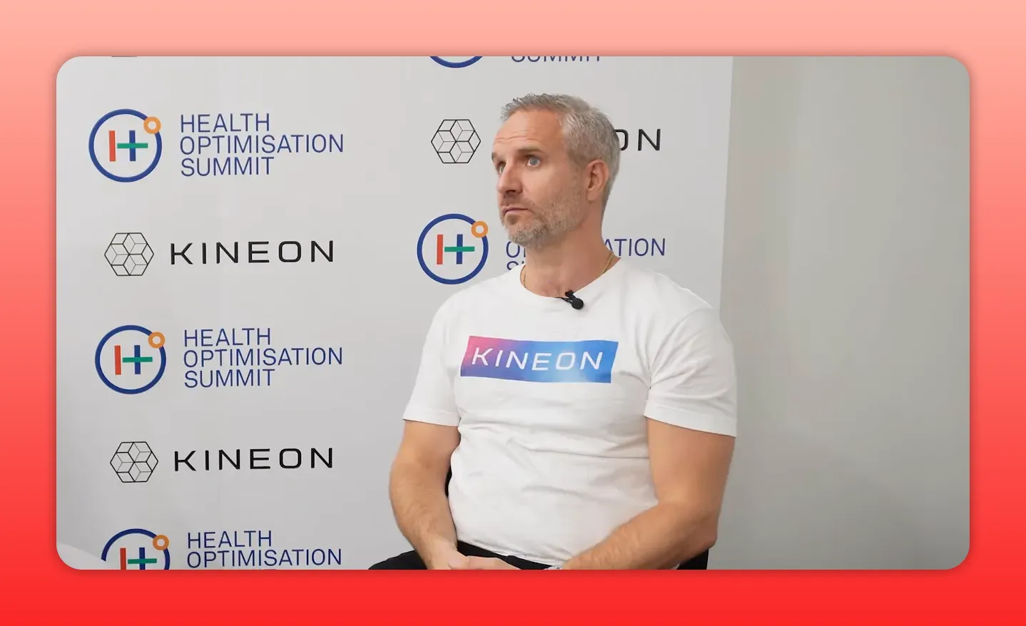Person in a Kineon t-shirt seated in front of a Health Optimisation Summit backdrop, listening and composed