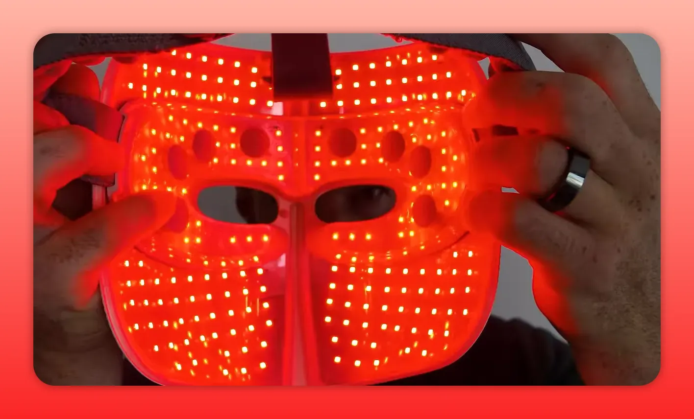 front view of a red light therapy mask interior showing dense red LEDs and eye openings held by hands