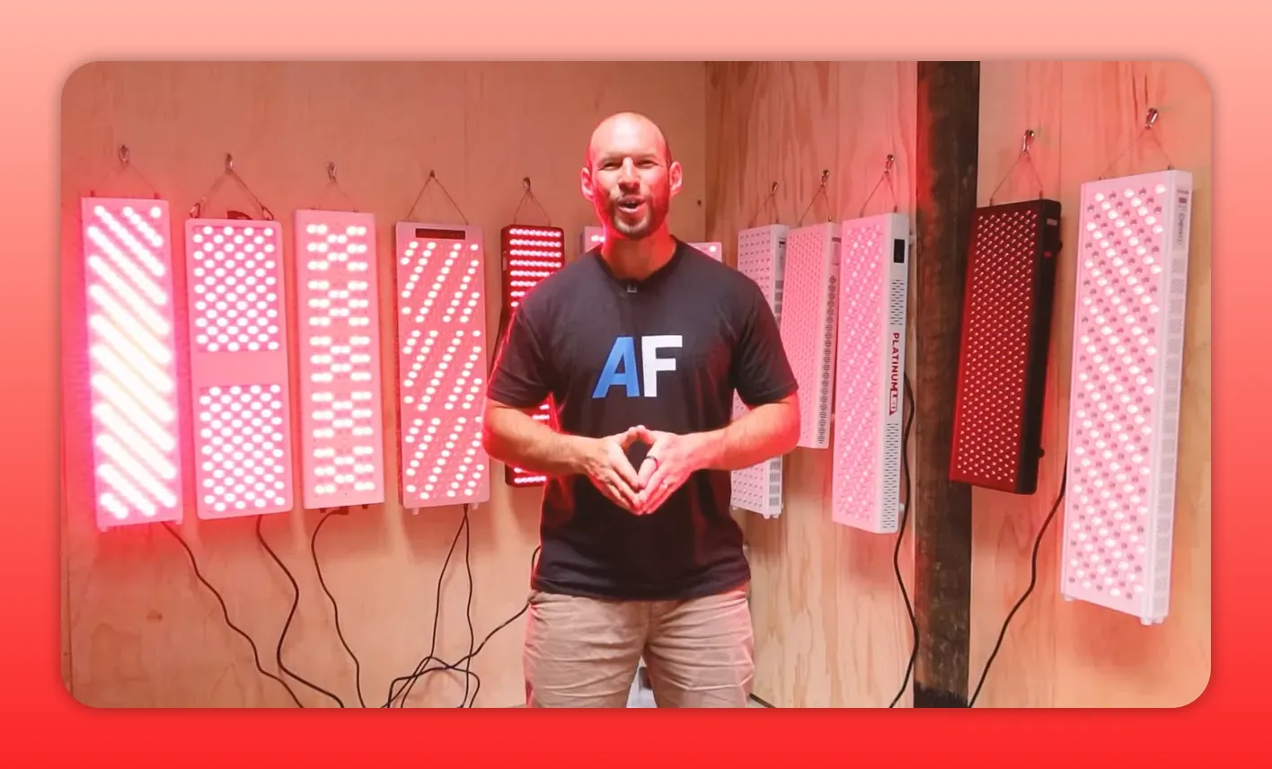 Presenter standing in front of multiple red light therapy panels mounted on a plywood wall