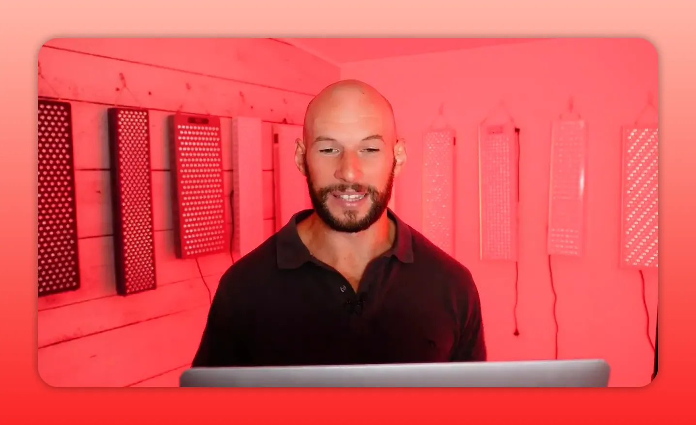 Wider shot showing presenter with multiple red light therapy LED panels mounted on the walls, illustrating device layout and coverage