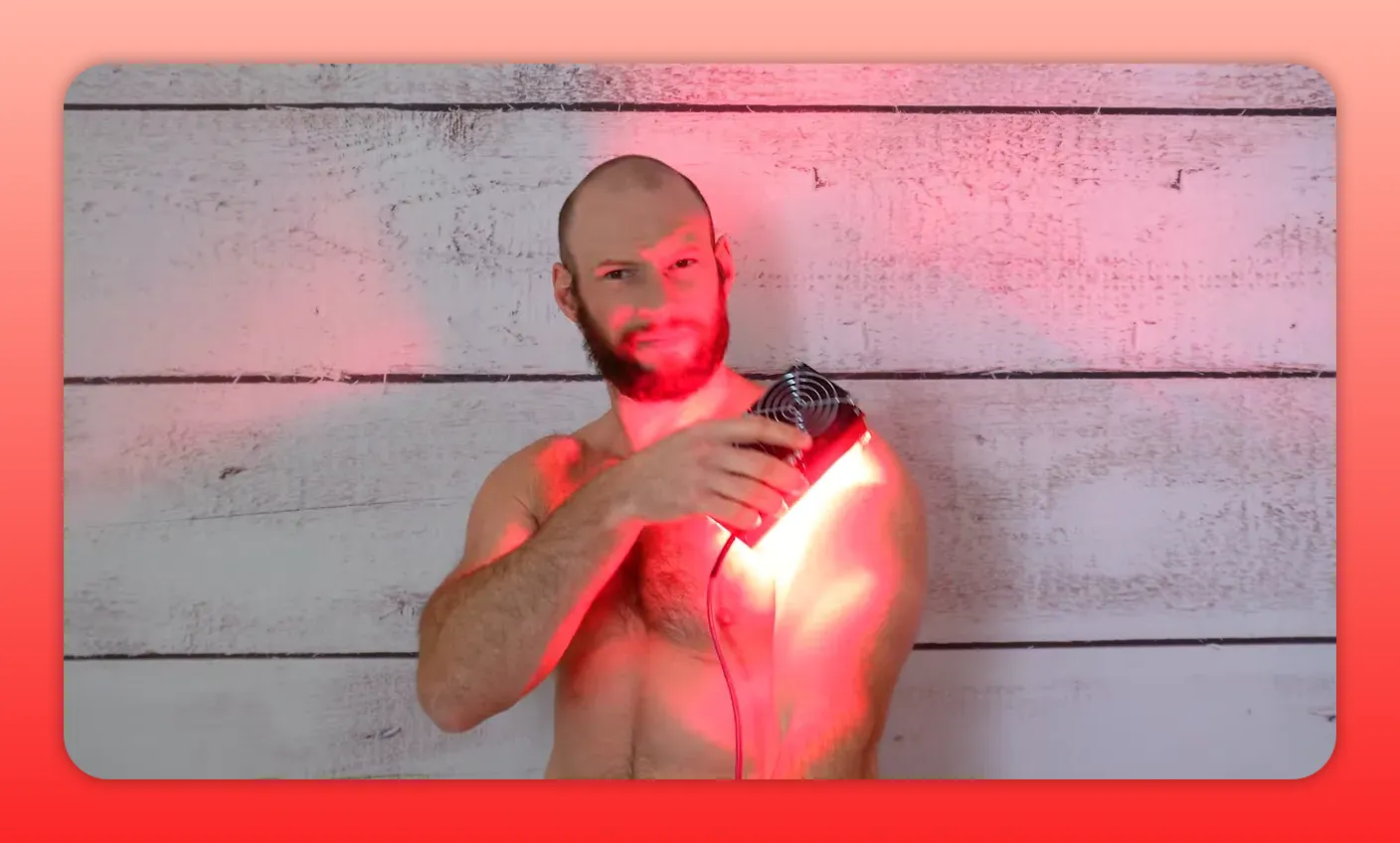 Person holding a compact handheld red light therapy device to the shoulder with strong red illumination