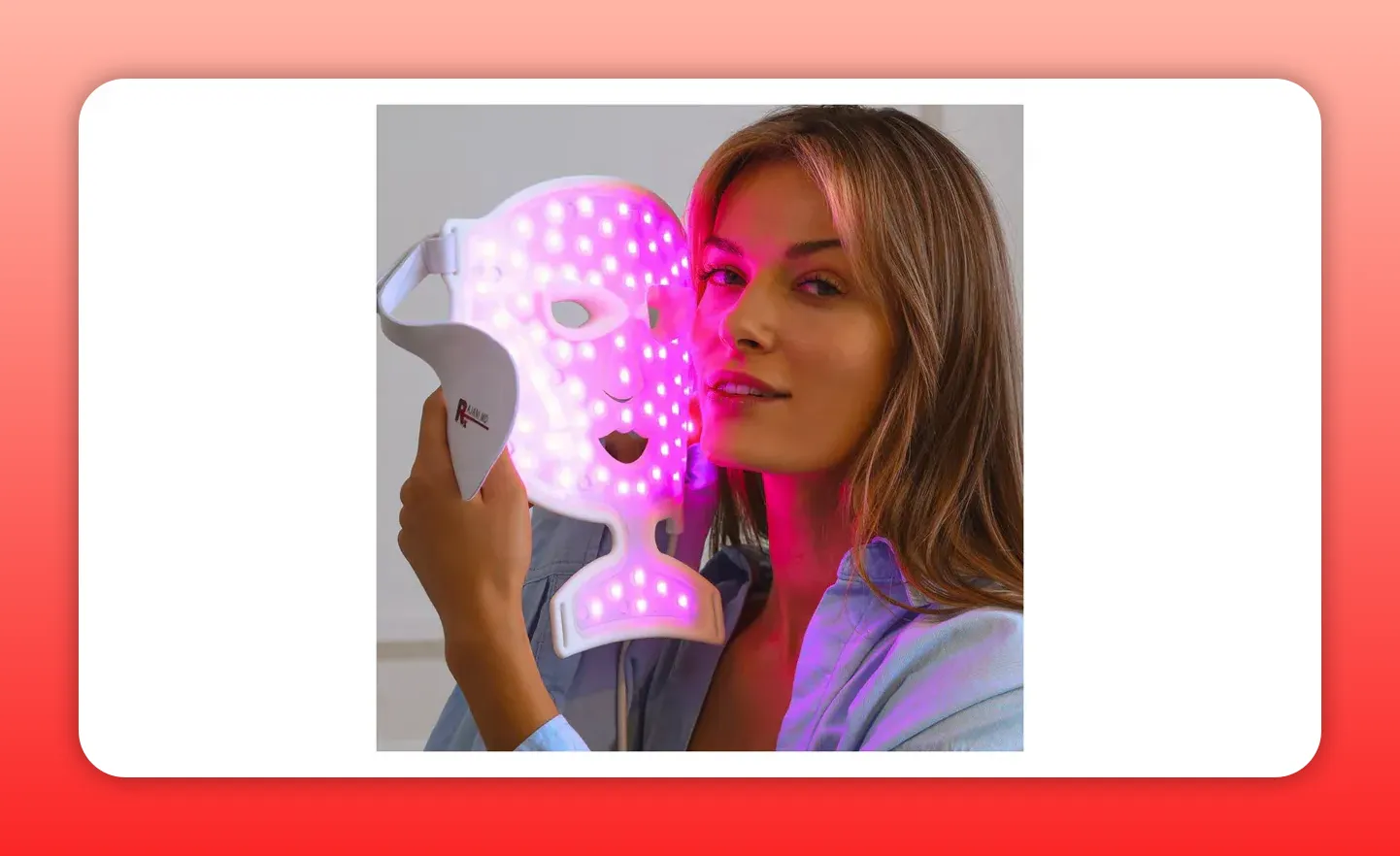 Hand-held LED facial mask glowing pink showing LED array and strap