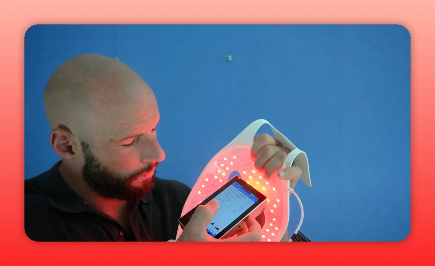 Person holding an illuminated red light therapy mask and checking readings on a handheld device