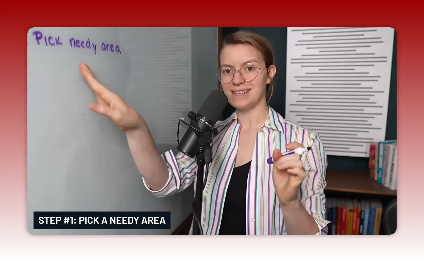 Presenter pointing to a whiteboard that reads 'Pick needy area' while holding a marker; microphone and on-screen label 'STEP #1: PICK A NEEDY AREA' are visible.