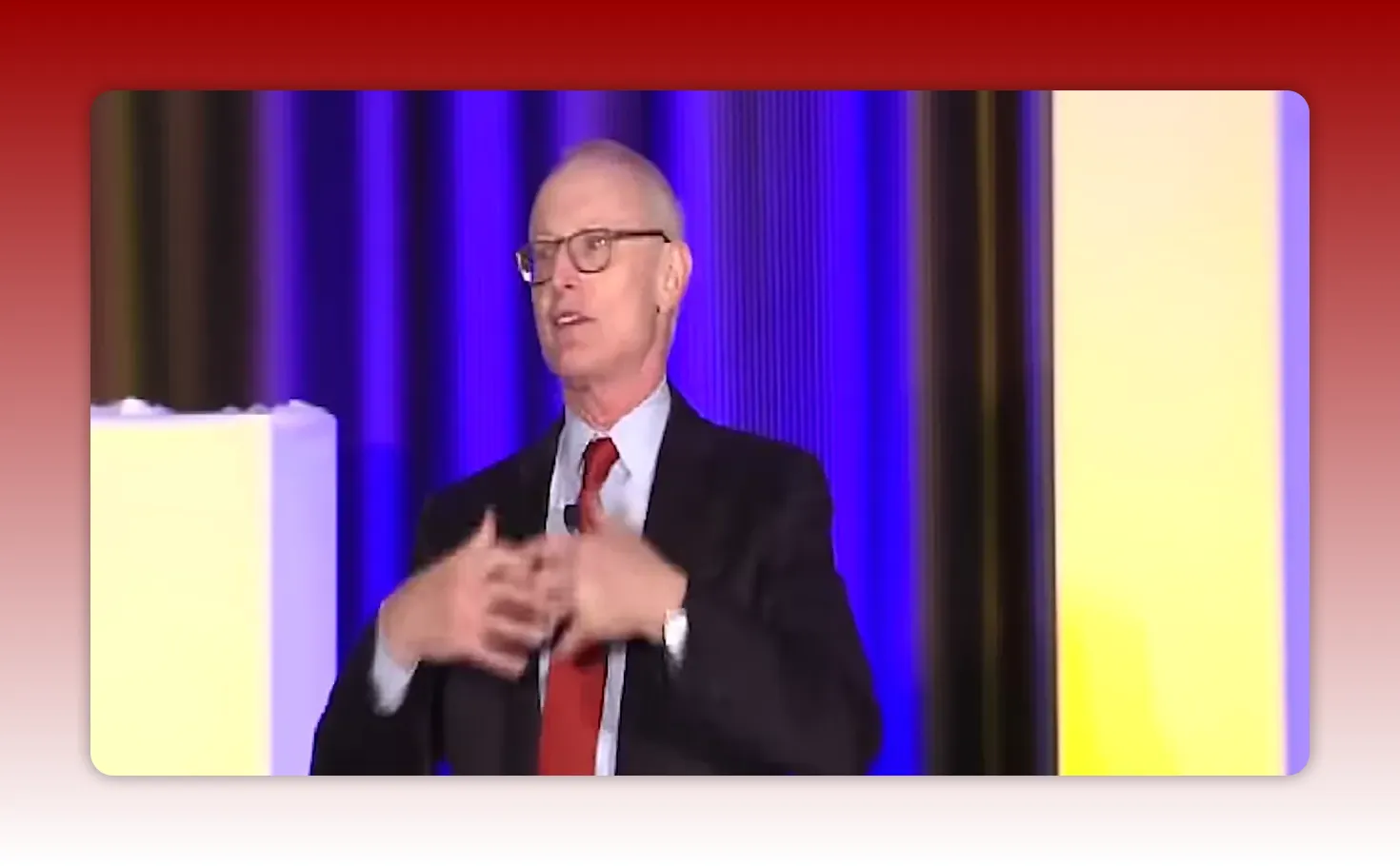 speaker on stage using clasped-hand gesture with colorful curtain backdrop, clear and sharp