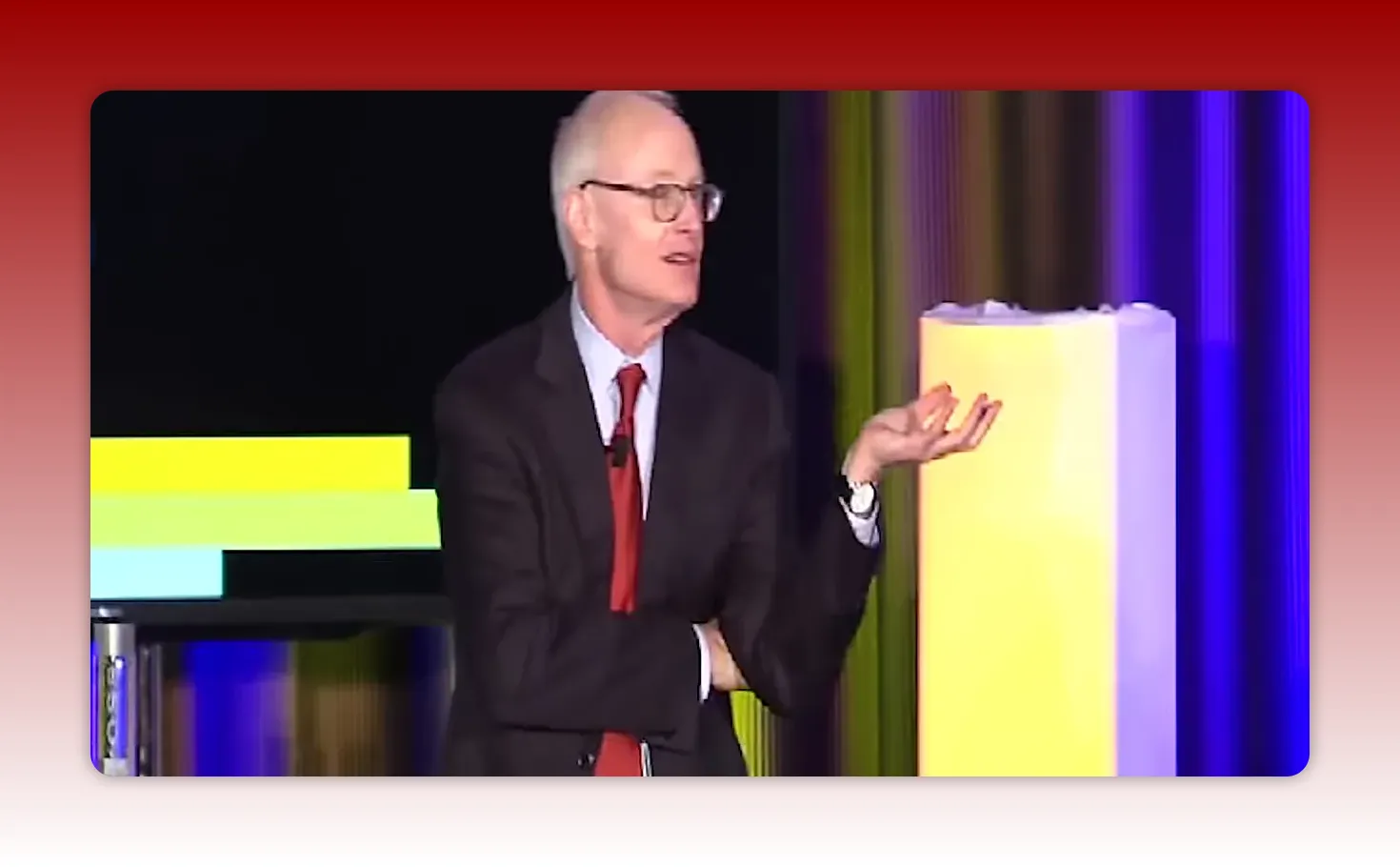 Presenter in suit with open-hand gesture beside a presentation screen showing horizontal colored bars and a vertical stage column