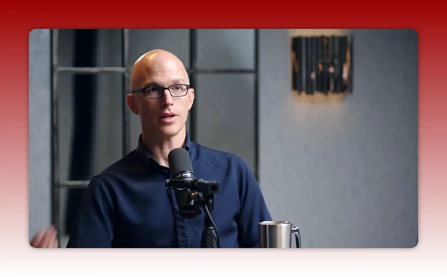 Speaker speaking into a podcast microphone with an attentive expression and studio background.
