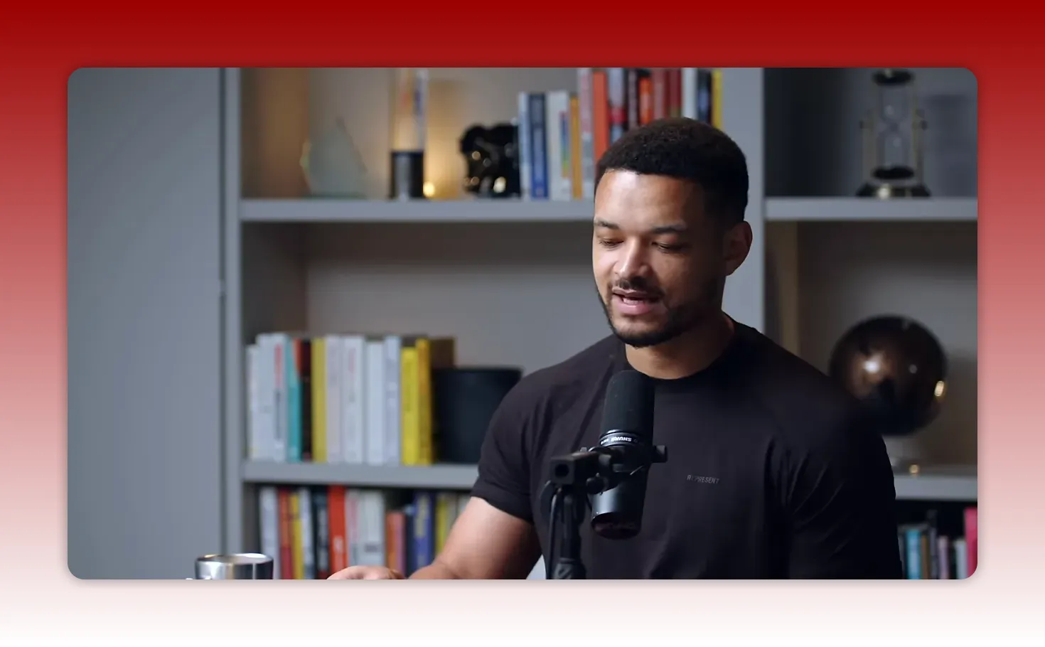 podcast guest looking down at notes and speaking into a microphone, bookshelf background