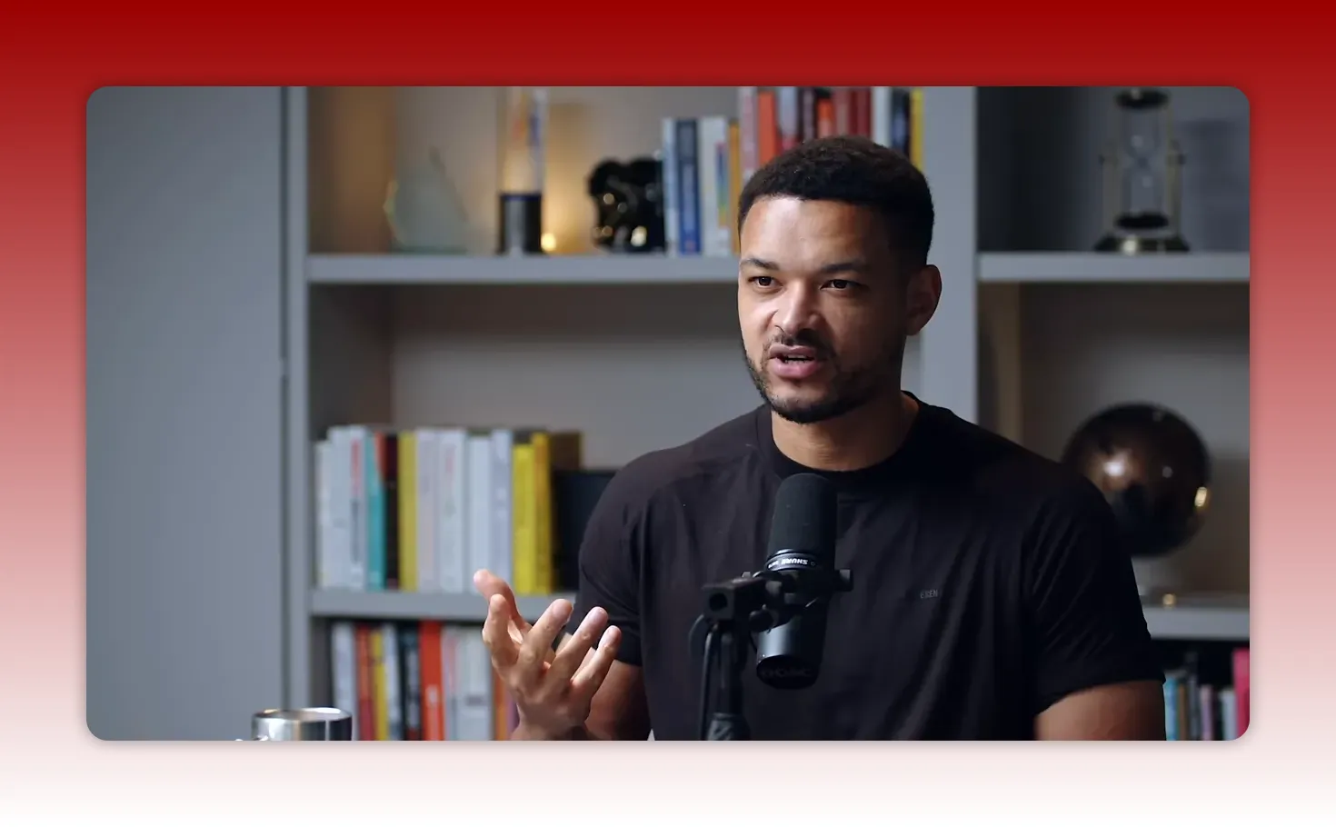 podcast host gesturing with hand while speaking into a microphone with bookshelf behind