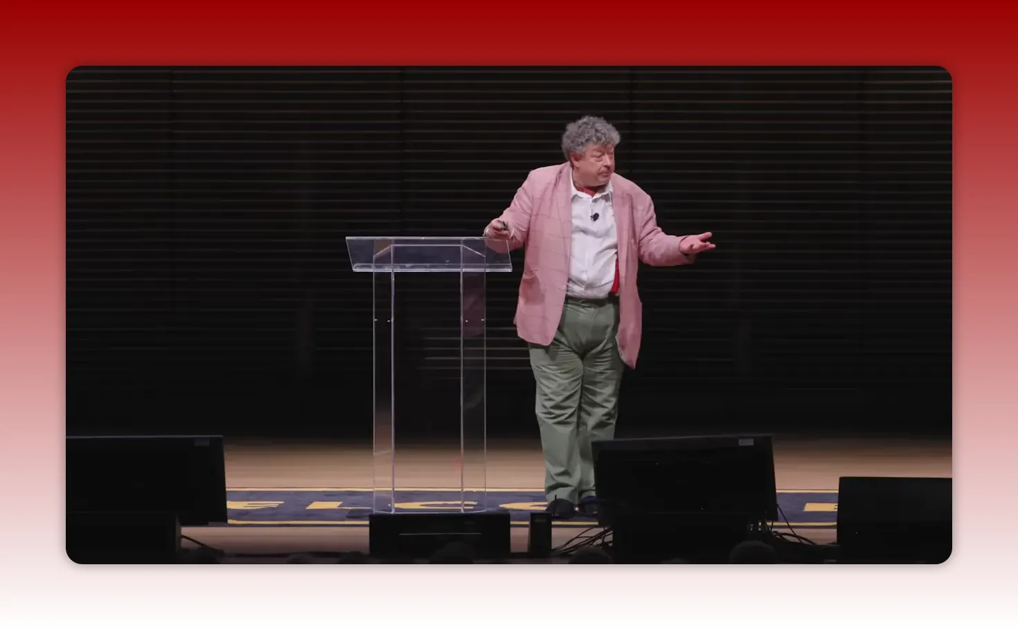 Speaker standing beside a clear lectern with an open-arm gesture on stage
