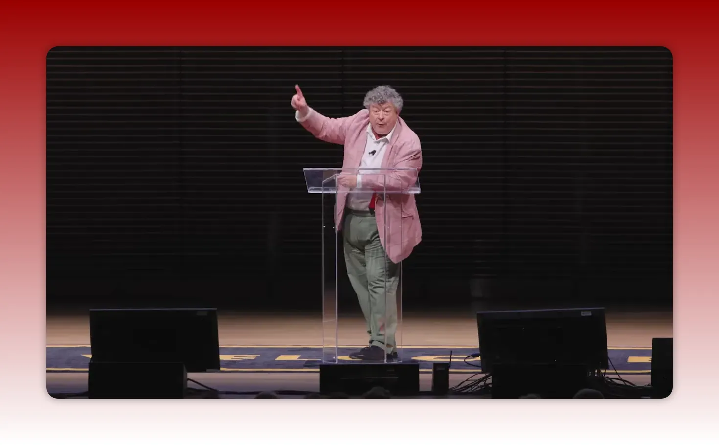 Speaker pointing upward from a clear lectern mid-sentence on stage