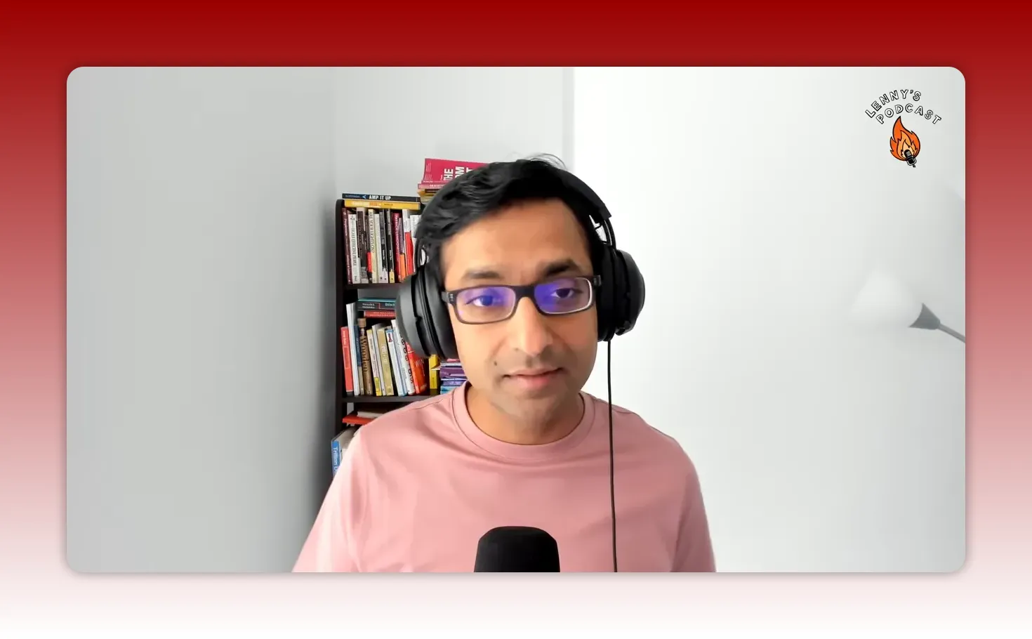 Podcast host centered in frame, clear focus with bookshelf and mic visible