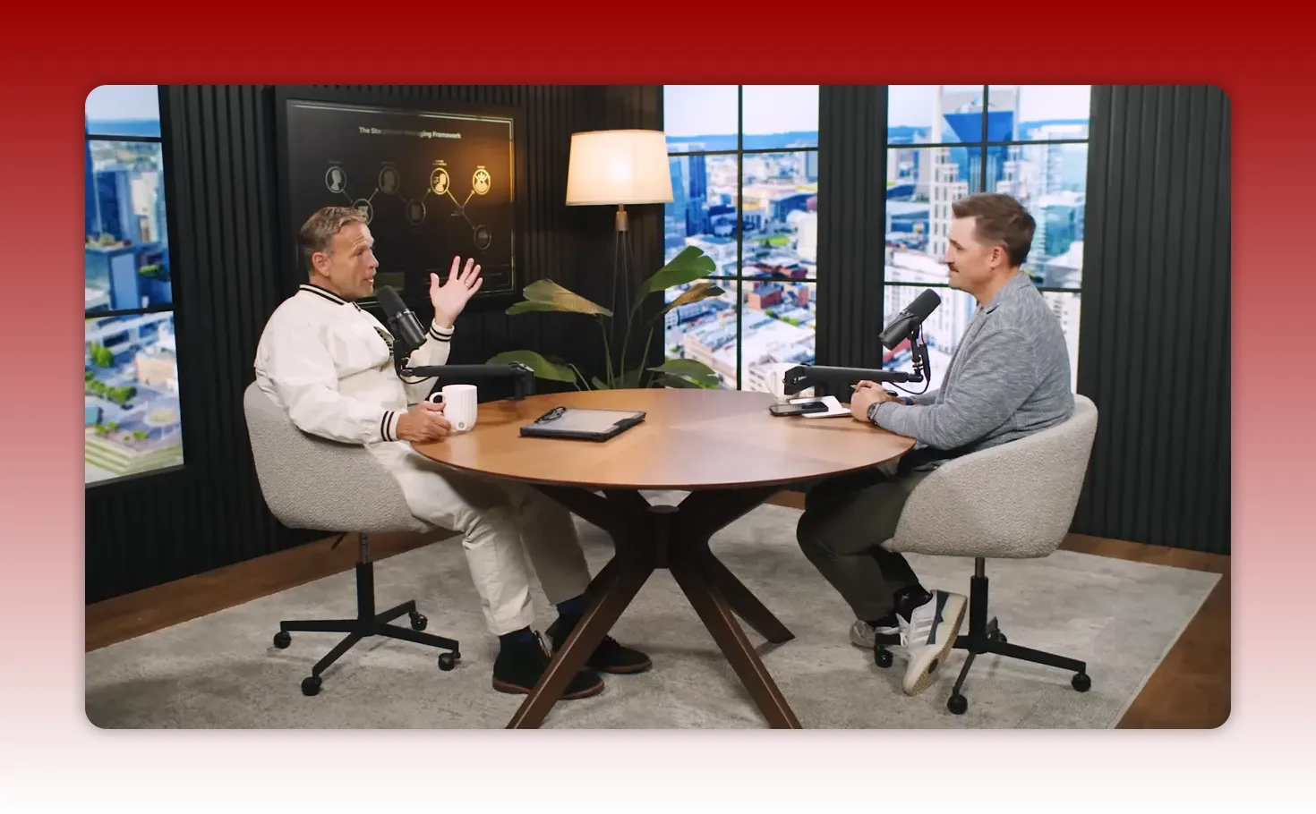 Wide studio shot of two hosts seated at a round table, microphones and a presentation screen visible as they discuss messaging.