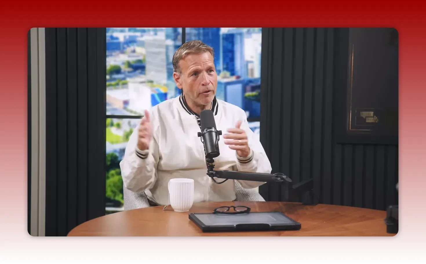 Podcast host facing the camera and speaking into a microphone while gesturing with both hands to illustrate a multi-step idea.