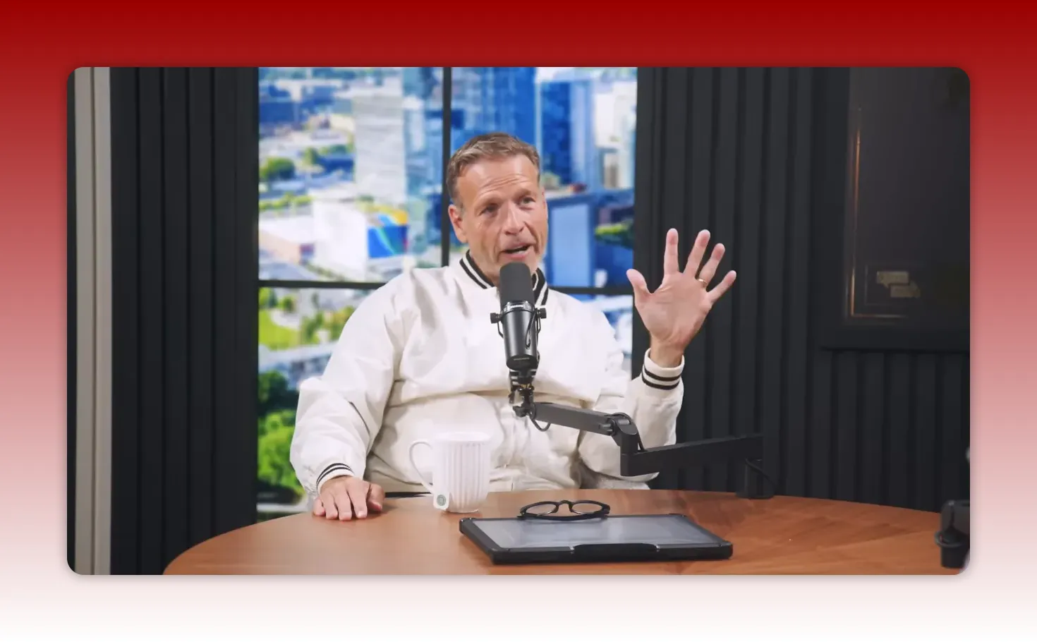 Podcast host speaking into a microphone with an open hand gesture, illustrating a point in a studio