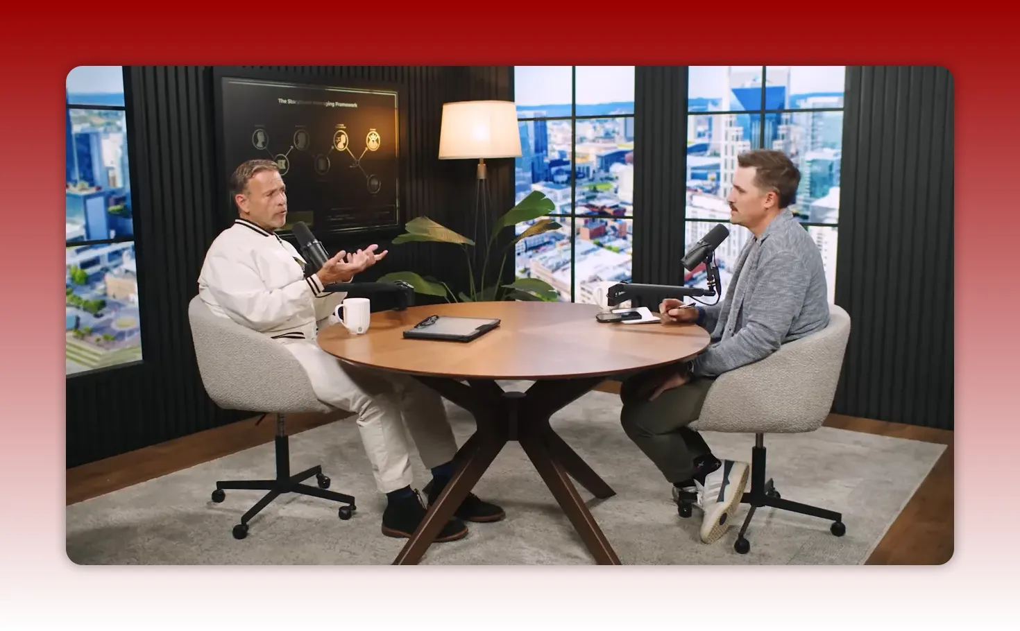 Two hosts in a podcast studio sitting at a round table discussing the framework with city-view windows behind them.