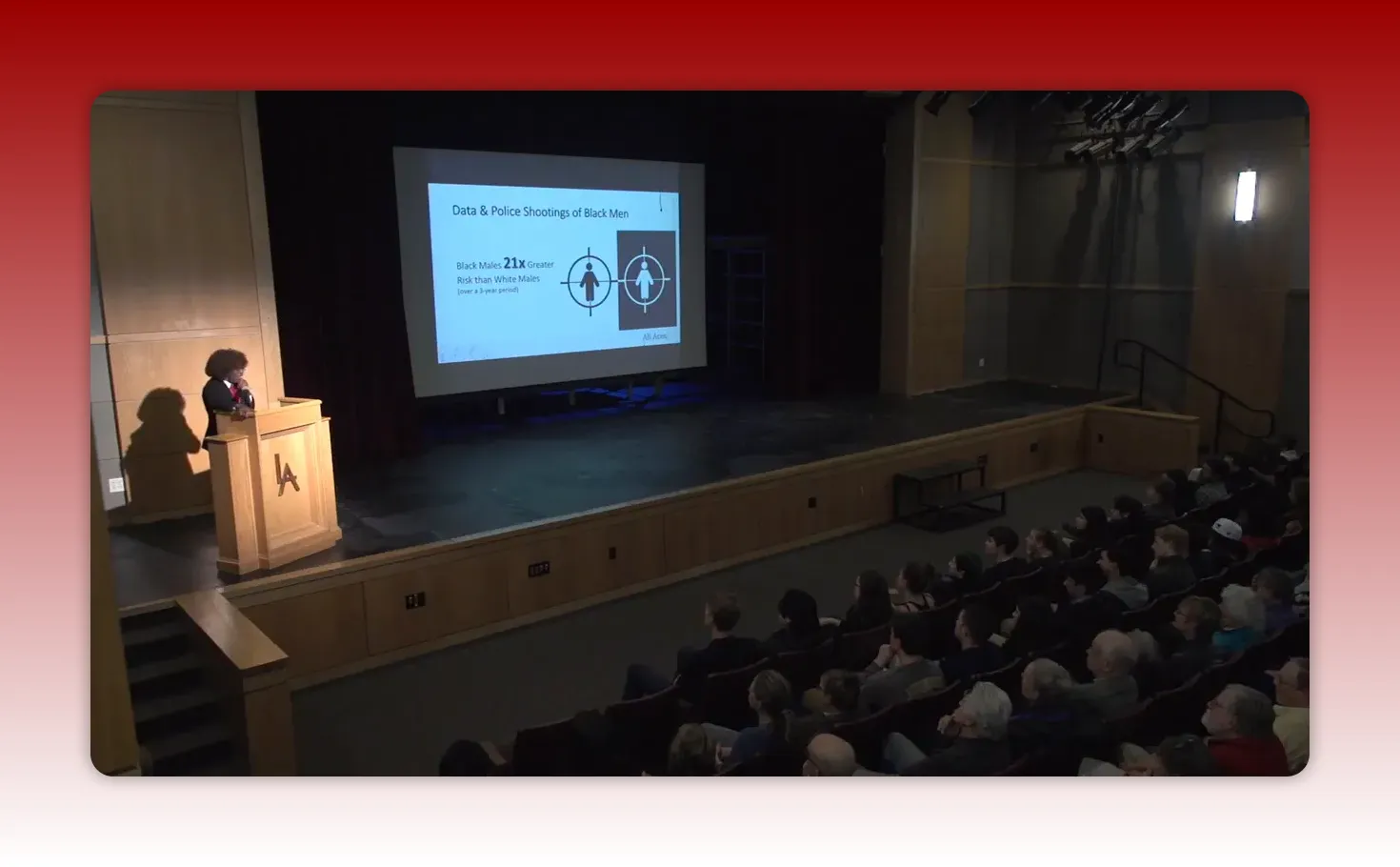 Presenter at podium with a slide titled 'Data & Police Shootings of Black Men' showing text that Black males face 21x greater risk than white males