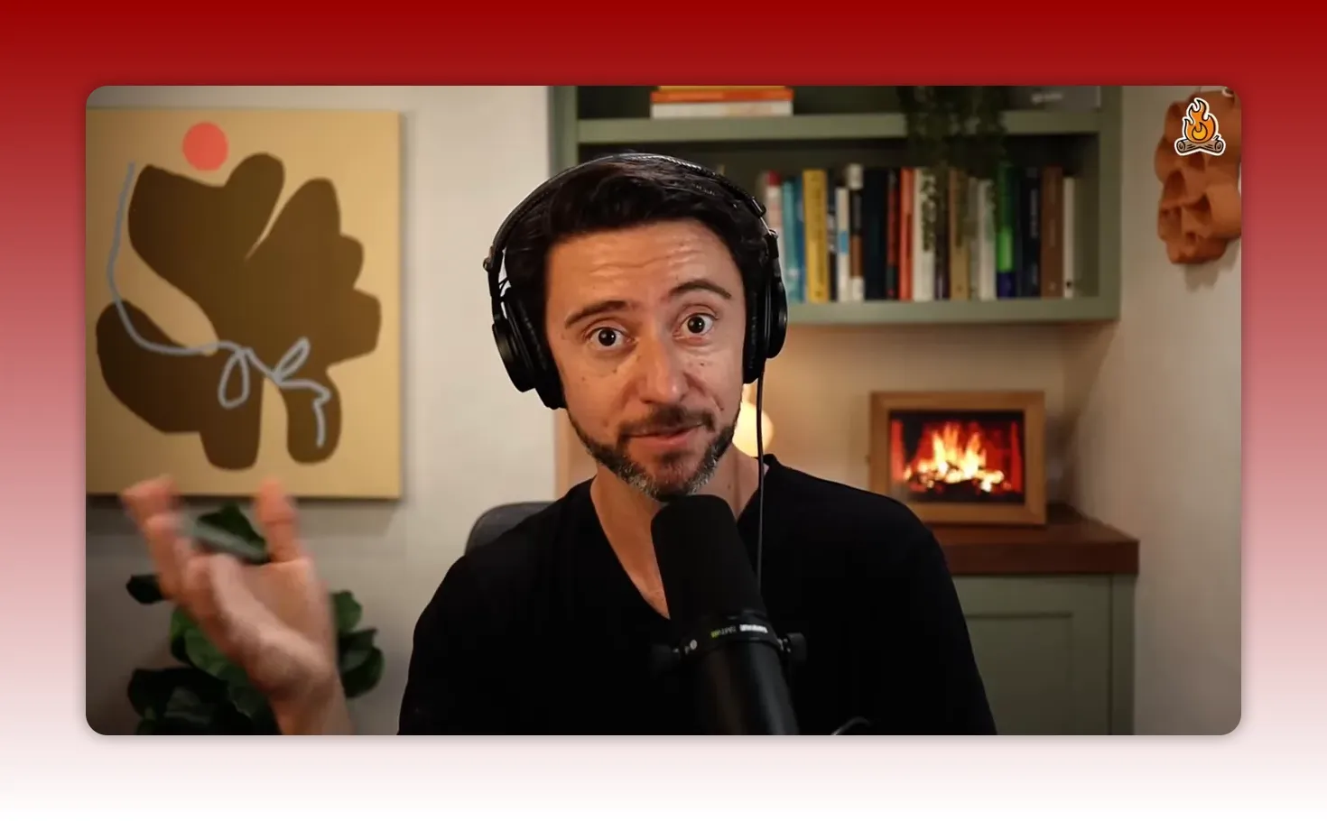 Podcast host speaking into a microphone with headphones on, gesturing with hand, bookshelf and decorative fireplace behind