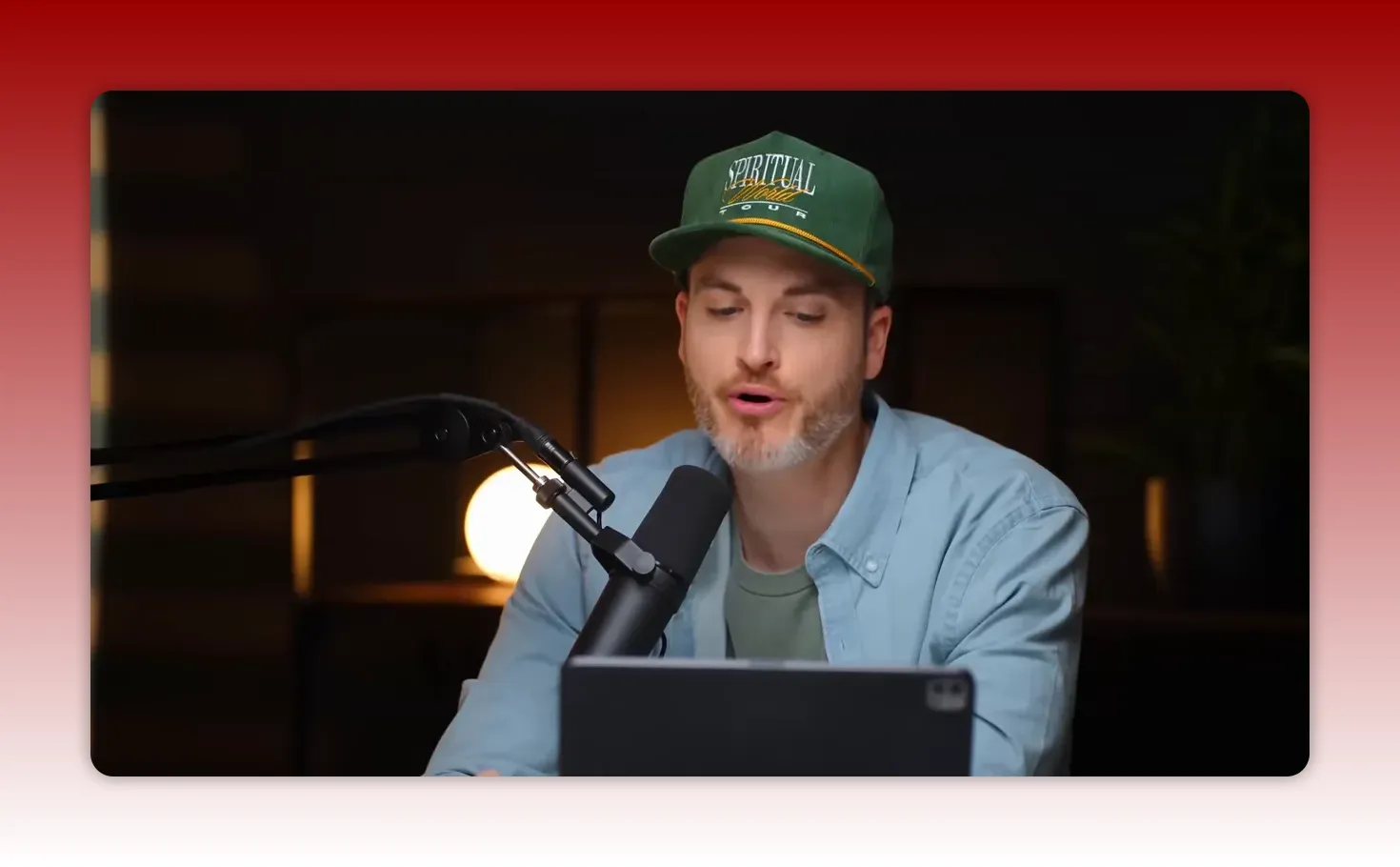 Creator leaning over a tablet with a studio microphone, appearing to read analytics or notes