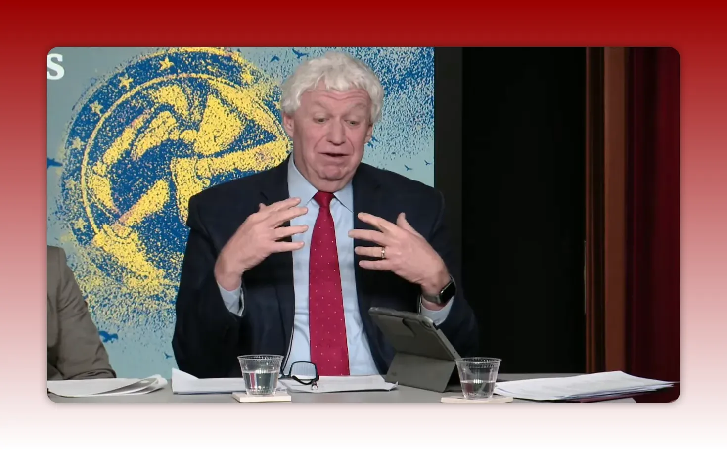 Panelist with both hands raised and fingers splayed, speaking at a preparedness panel, illustrative of explaining a clinical technique.