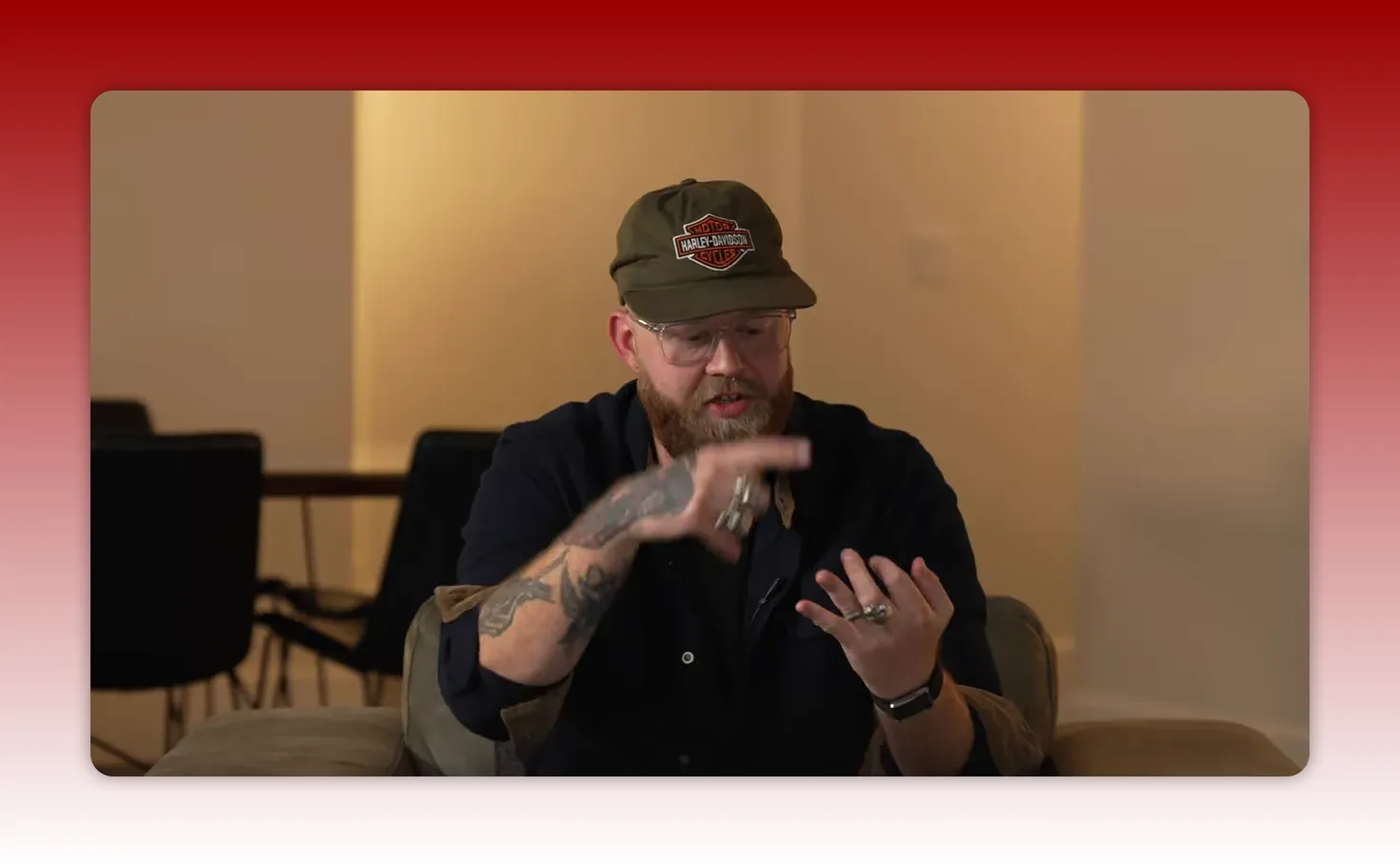 Presenter seated on a couch, using hand gestures to count points while speaking in a home-studio set
