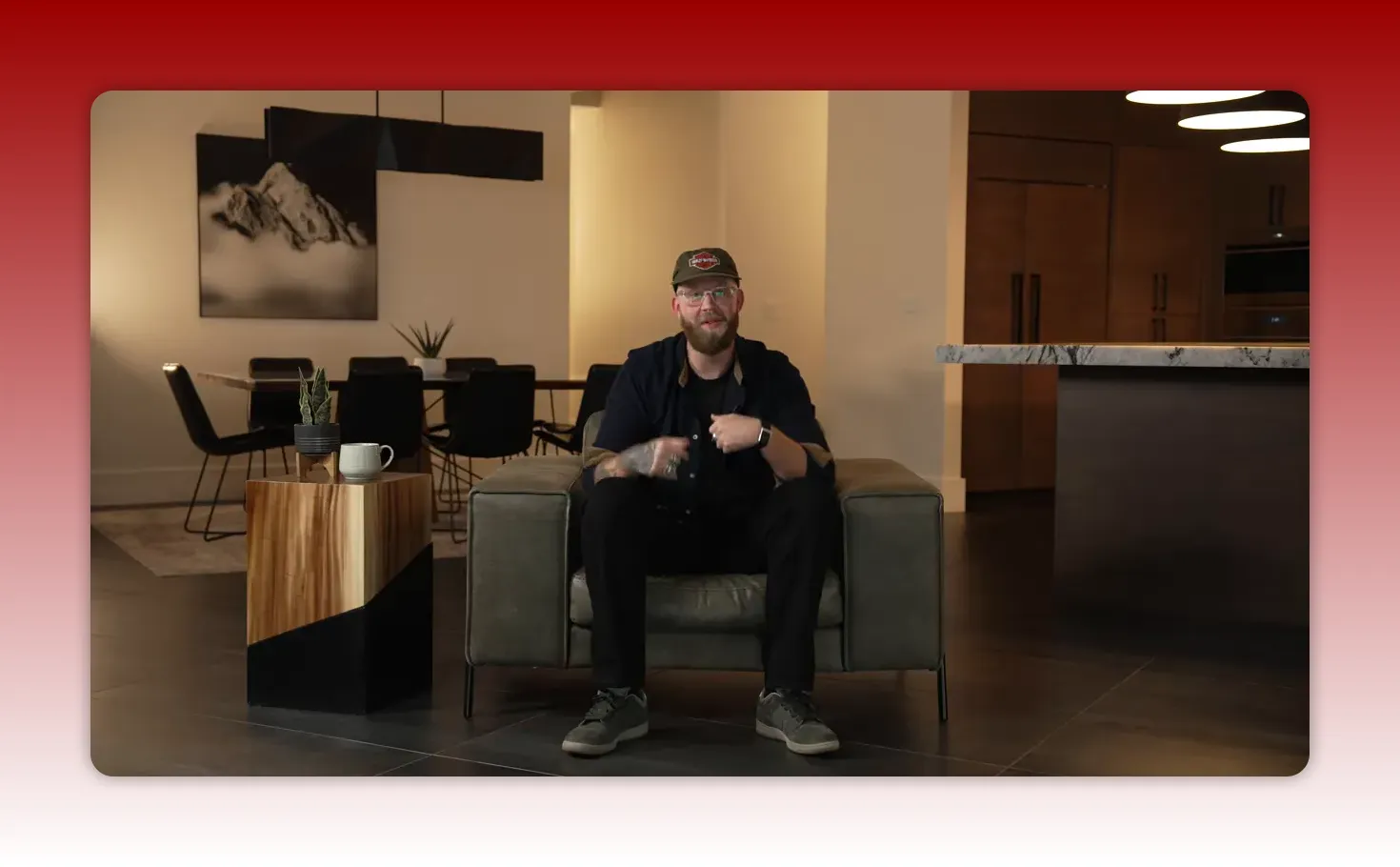 Wide shot of a speaker seated in a modern living-room/kitchen set — clear, well-lit, and centered.