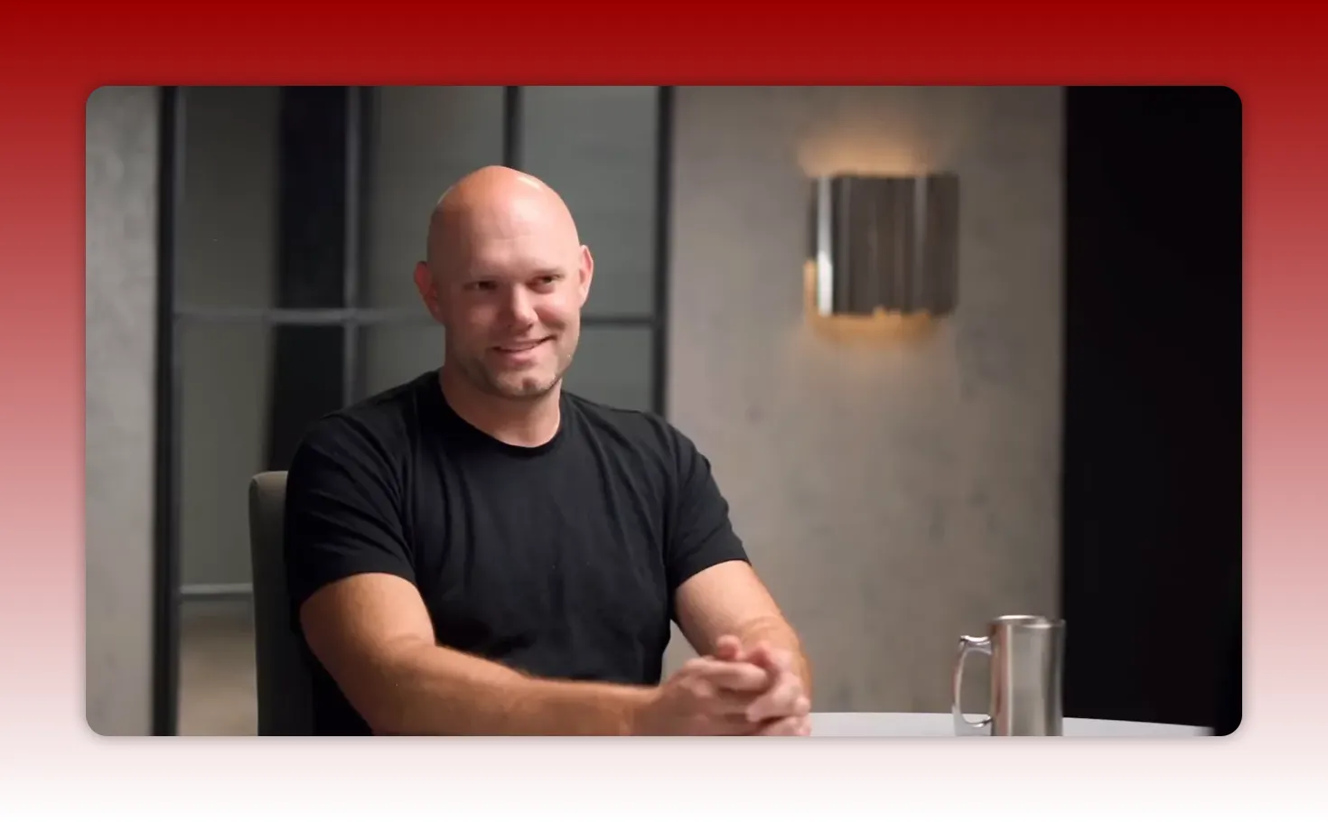 smiling man in black t-shirt with hands clasped at a table, friendly interview shot