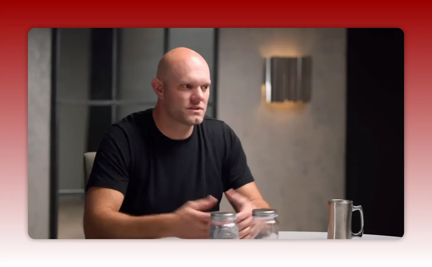 Presenter using hand gestures over two glass jars on a table beside a metal mug, showing a physical habit-tracking example.