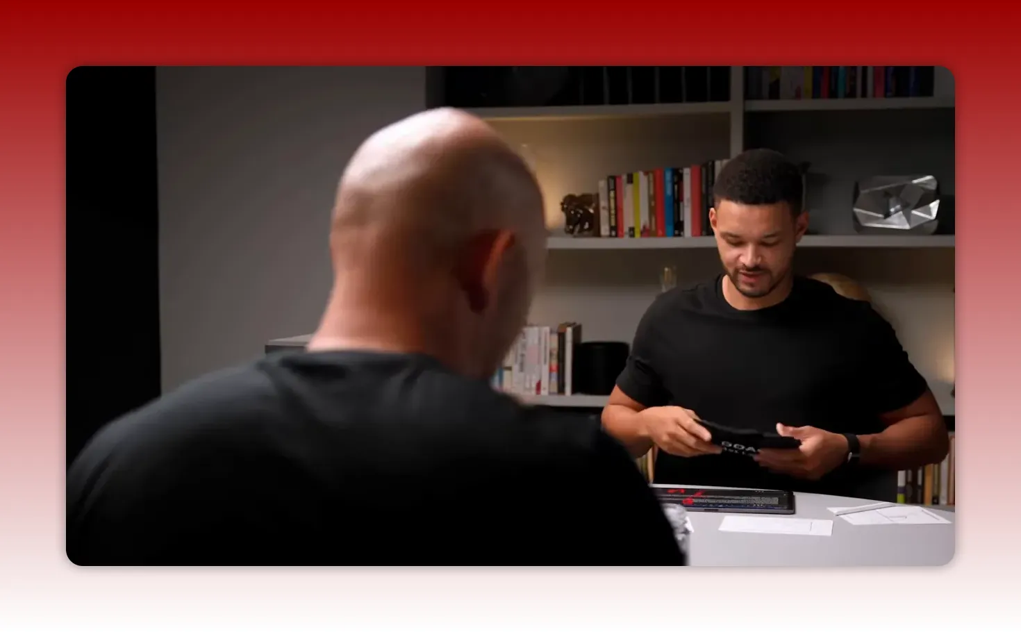 Two people at a round table in an office setting with bookshelves and visible materials, showing environmental cues and a shared workspace.