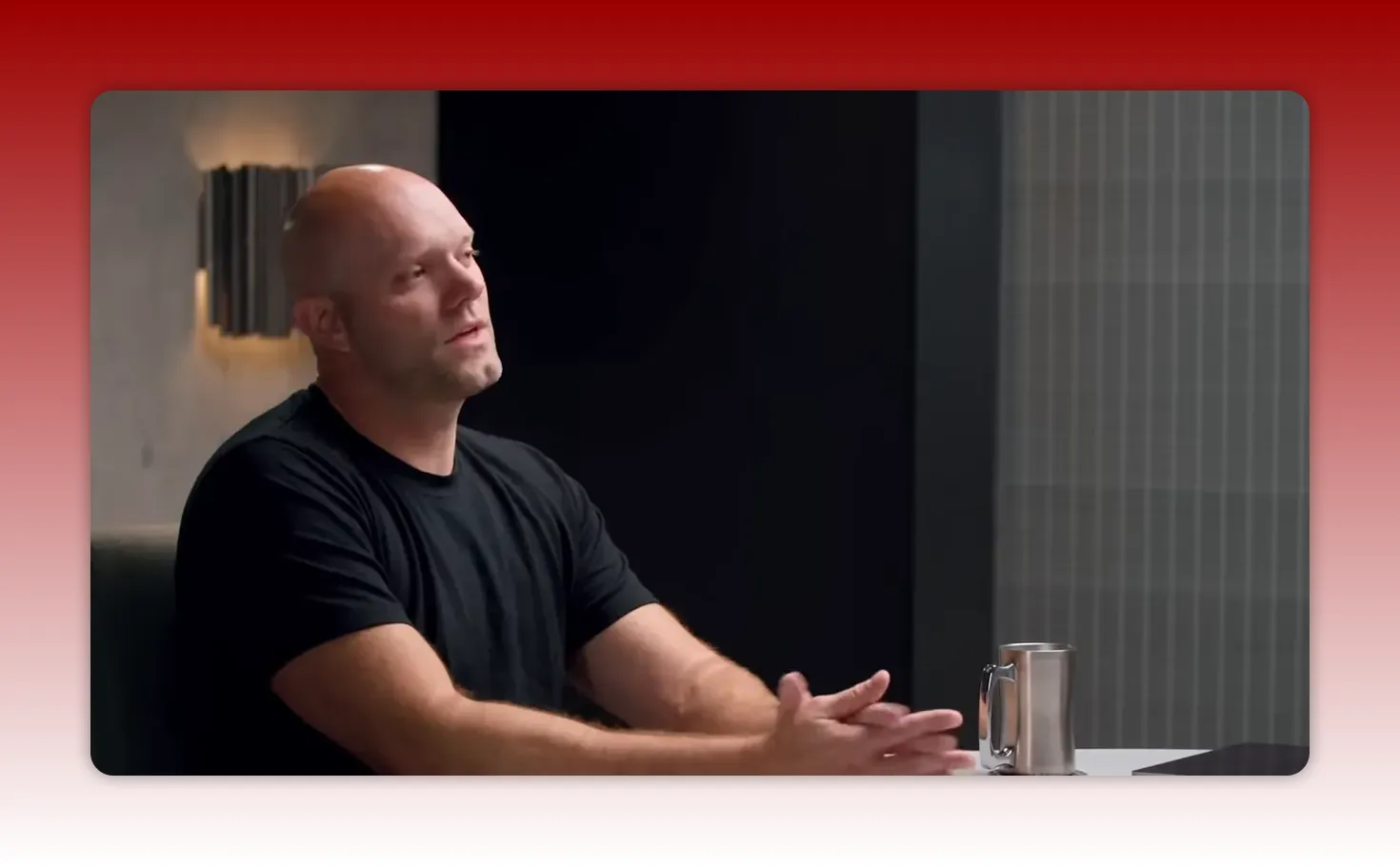 Presenter in black t-shirt gesturing with hands at a table with a metal mug visible