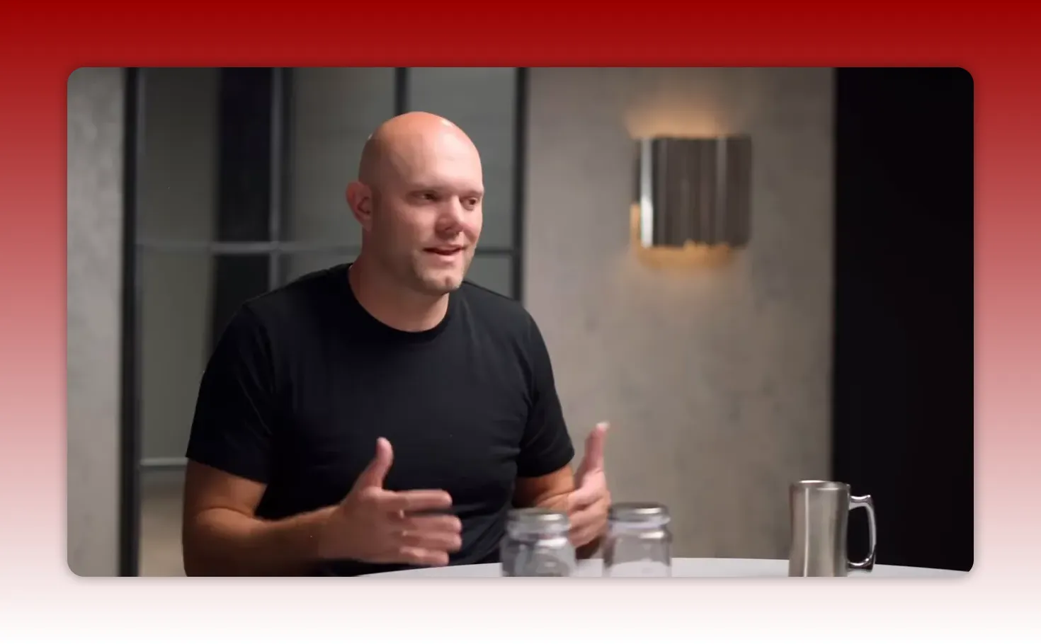Smiling speaker using hand gestures with two glass jars and a metal mug on the table, illustrating a tangible habit-tracking method.