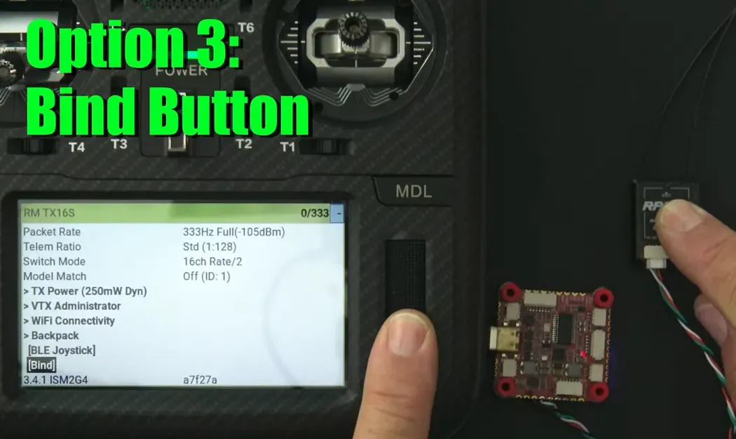 Finger pressing the ExpressLRS receiver's bind button with the flight controller and TX16S radio visible — demonstration of the receiver bind action