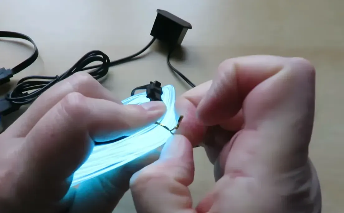 clear close-up of hands holding glowing coiled EL wire with small inverter and USB cable in background