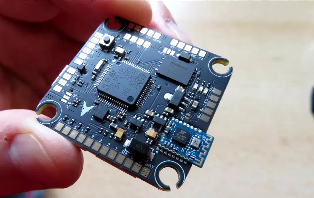 Velox F7 SE flight controller top view showing STM MCU, silkscreen pads and small Bluetooth module