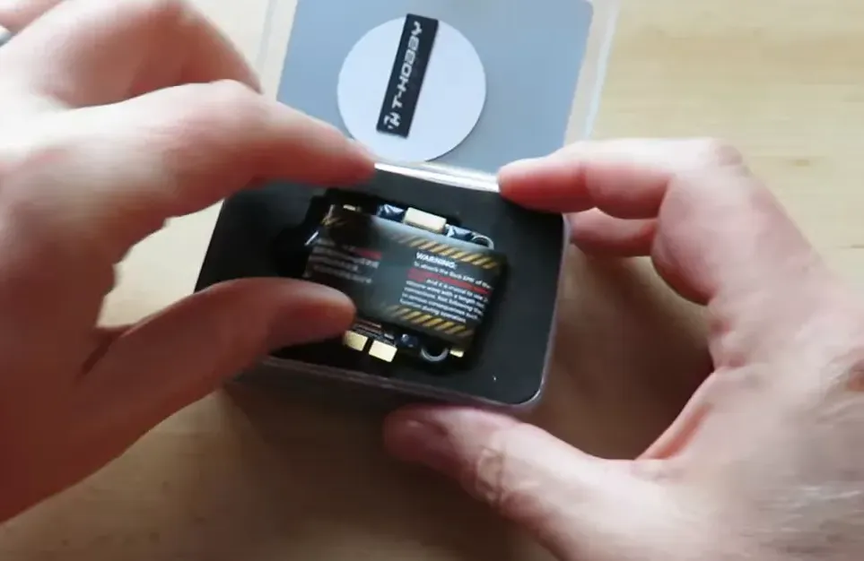 Velox V70A SE 4-in-1 ESC visible in foam tray inside metal tin with hands for scale