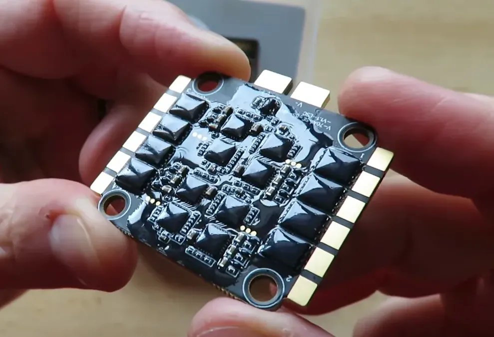 Top view of V70A 4-in-1 ESC held between hands showing MOSFETs, solder pads and mounting holes
