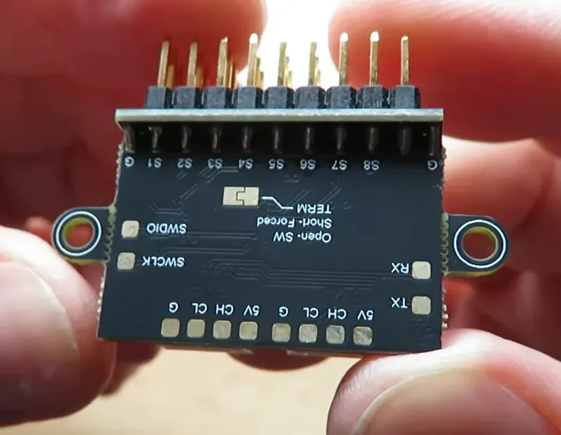 TBS DroneCAN PWM board back showing S1–S8 labels, 5V/CH pads and JST ports held between fingers