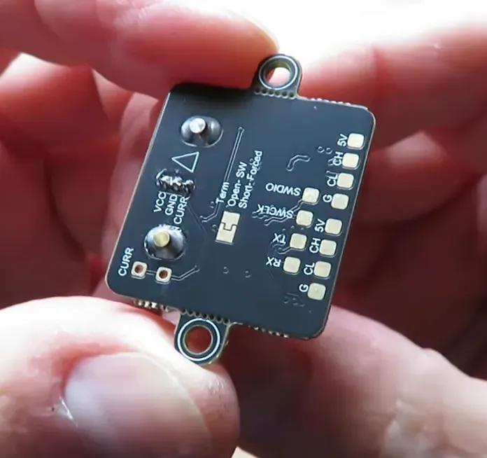 TBS sensor PCB with labelled SWD, TX/RX and CAN/I2C pads held between fingers