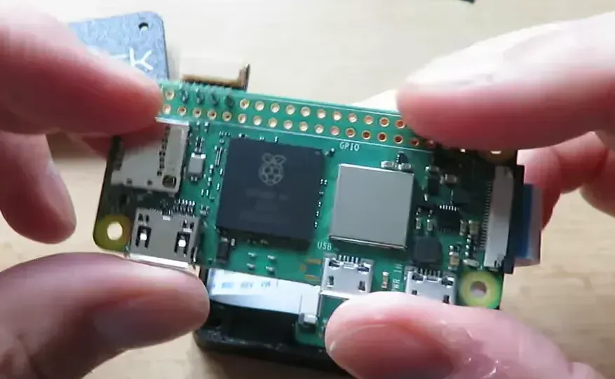 Close-up view of a Raspberry Pi board with camera ribbon and USB ports being held above the Landmark enclosure