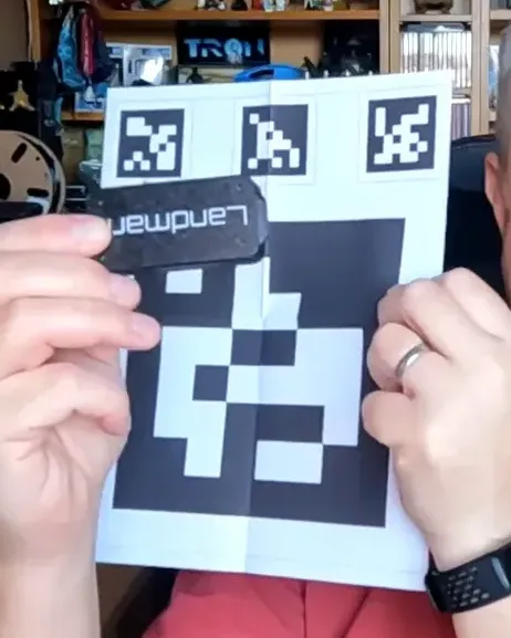 Person holding a printed AprilTag landing target with the Landmark vision unit next to it