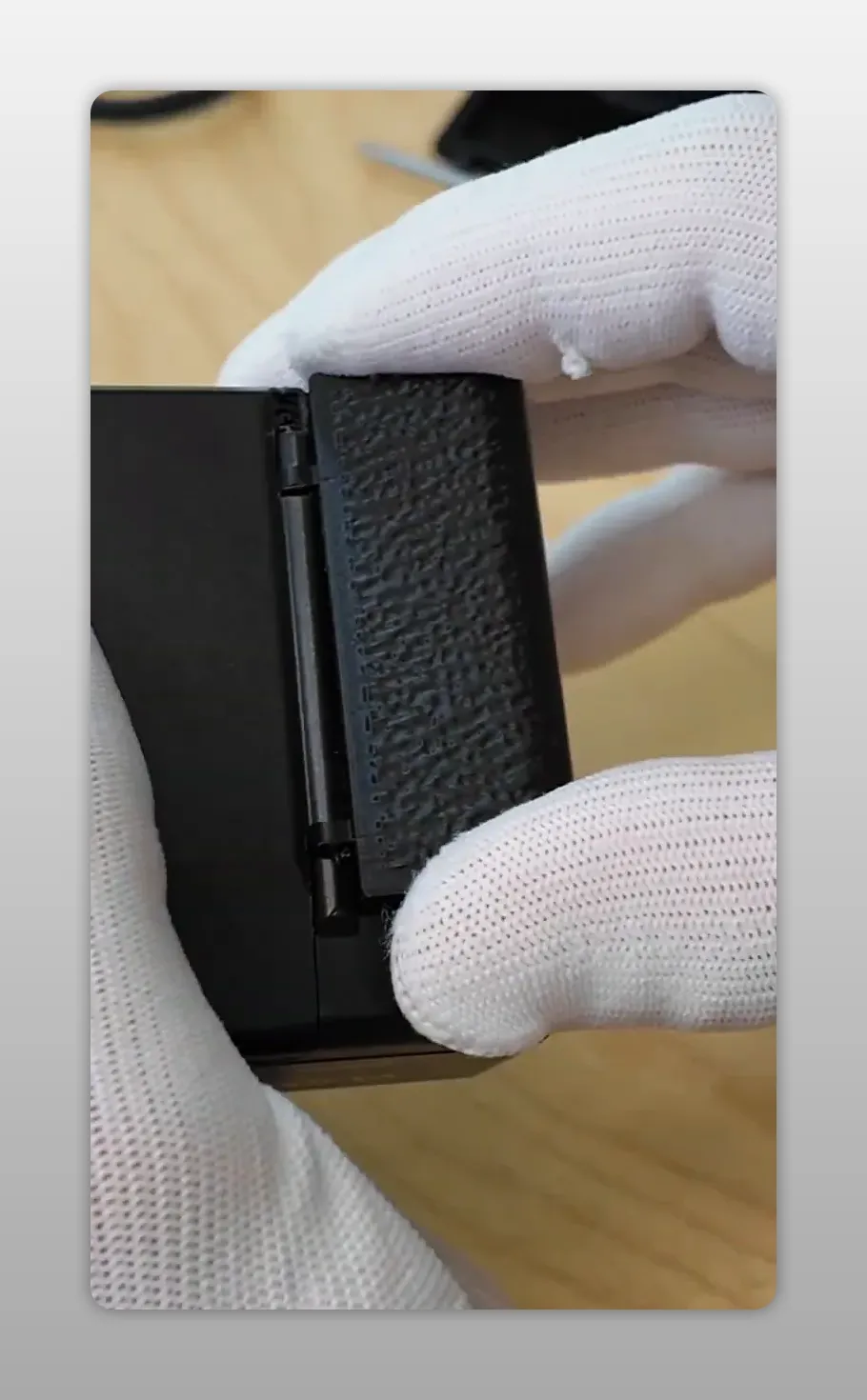 Mains gantées tenant un Yashica T3 avec le couvercle de compartiment batterie de rechange enclenché, montrant la finition texturée