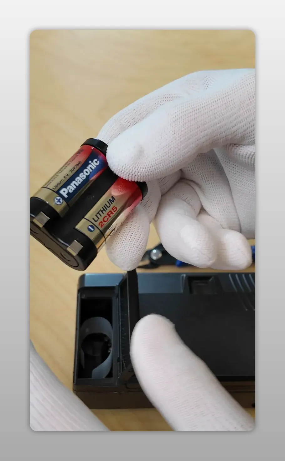 Main gantée tenant une pile Panasonic 2CR5 prête à être insérée dans le compartiment batterie ouvert du Yashica T3