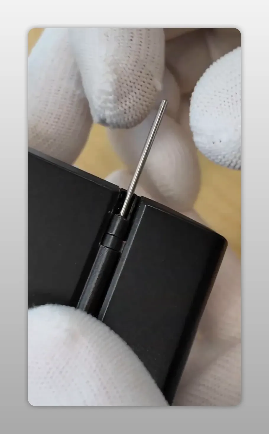 La goupille est réinsérée dans la charnière du compartiment batterie du Yashica T3 lors du remontage