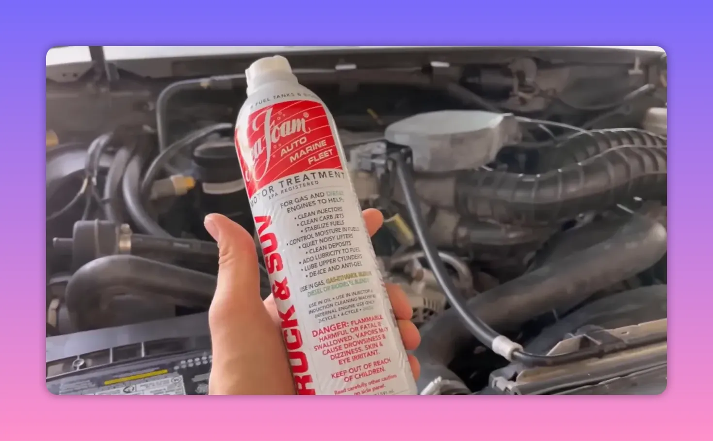 Hand holding a can of Seafoam Motor Treatment in front of an open engine bay