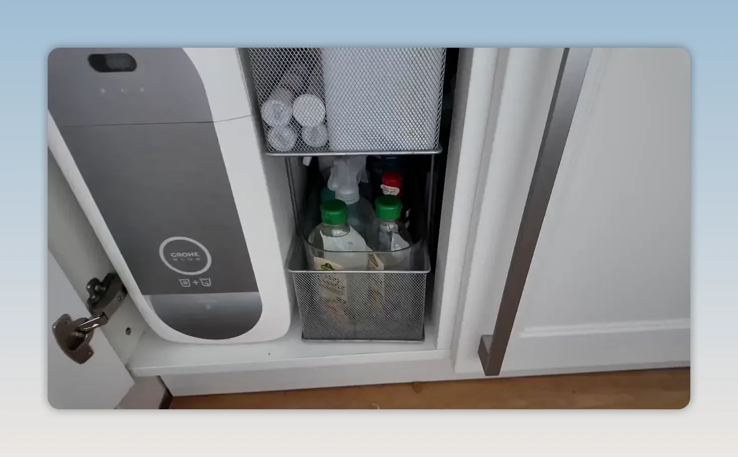 Geöffneter Unterschrank mit Reinigungsflaschen und Putzmitteln neben einem Waschbecken