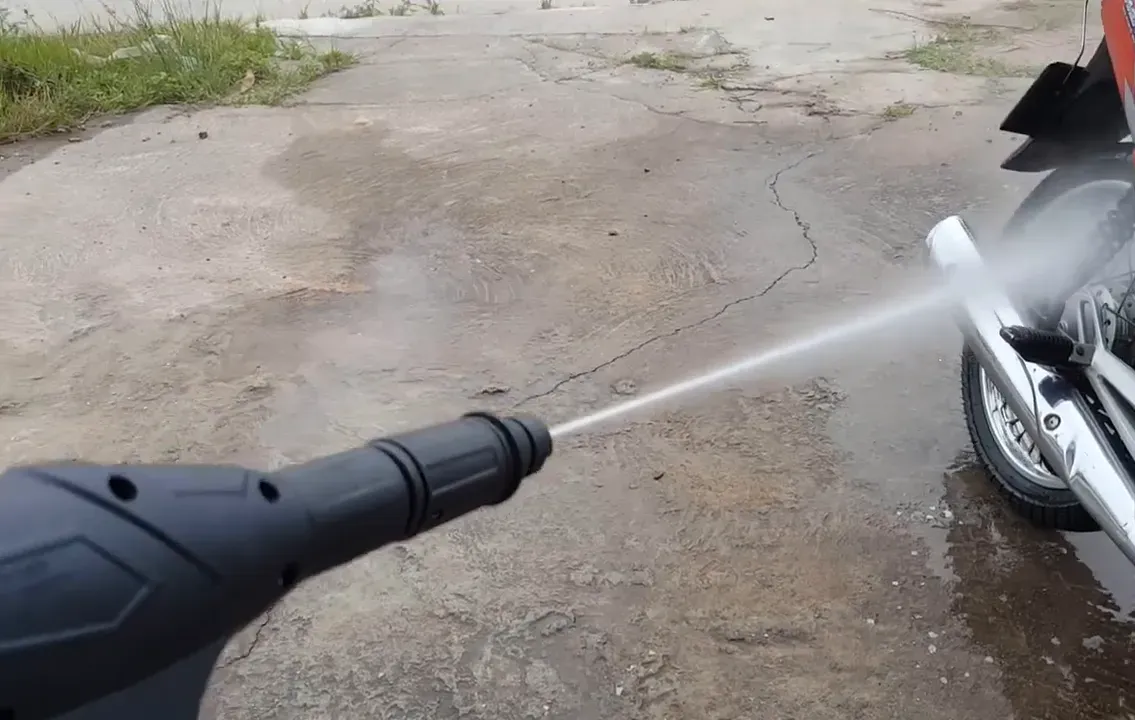 Máy rửa xe đang phun tia nước mạnh vào khu vực ống xả và gầm xe máy