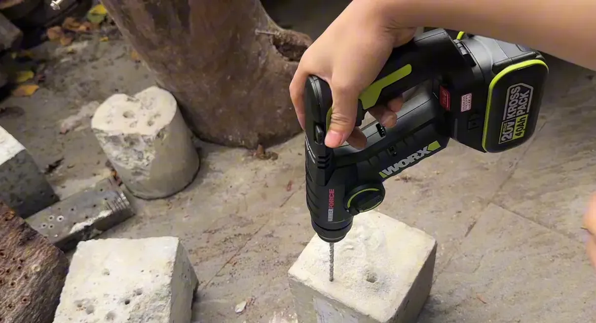 Máy khoan pin Worx đang khoan một lỗ nhỏ trên khối bê tông, mũi khoan thẳng, tay người cầm máy.