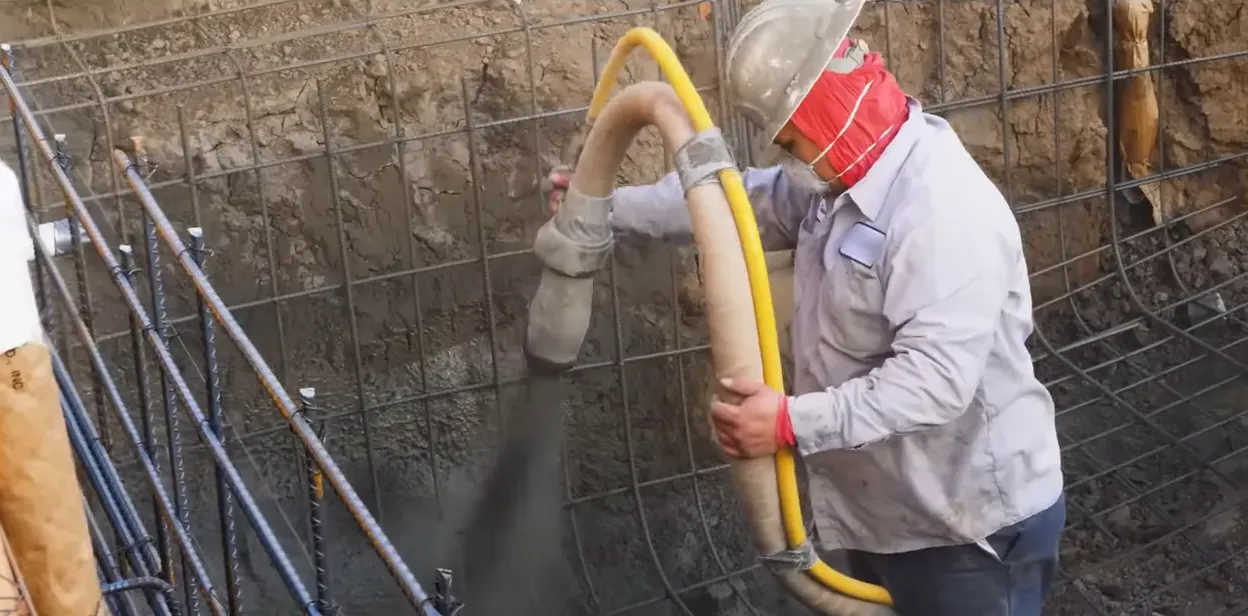 crew member using a high-pressure shotcrete hose to apply gunite to a pool rebar wall