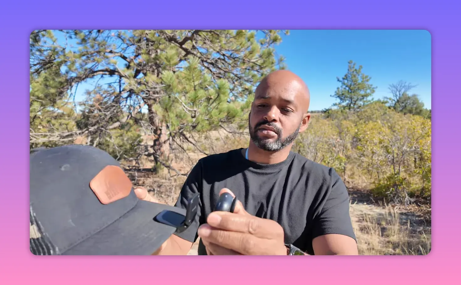 Person outdoors holding an insta360 Go Ultra and the easy-clip next to a hat bill, demonstrating how the clip mounts to the hat.