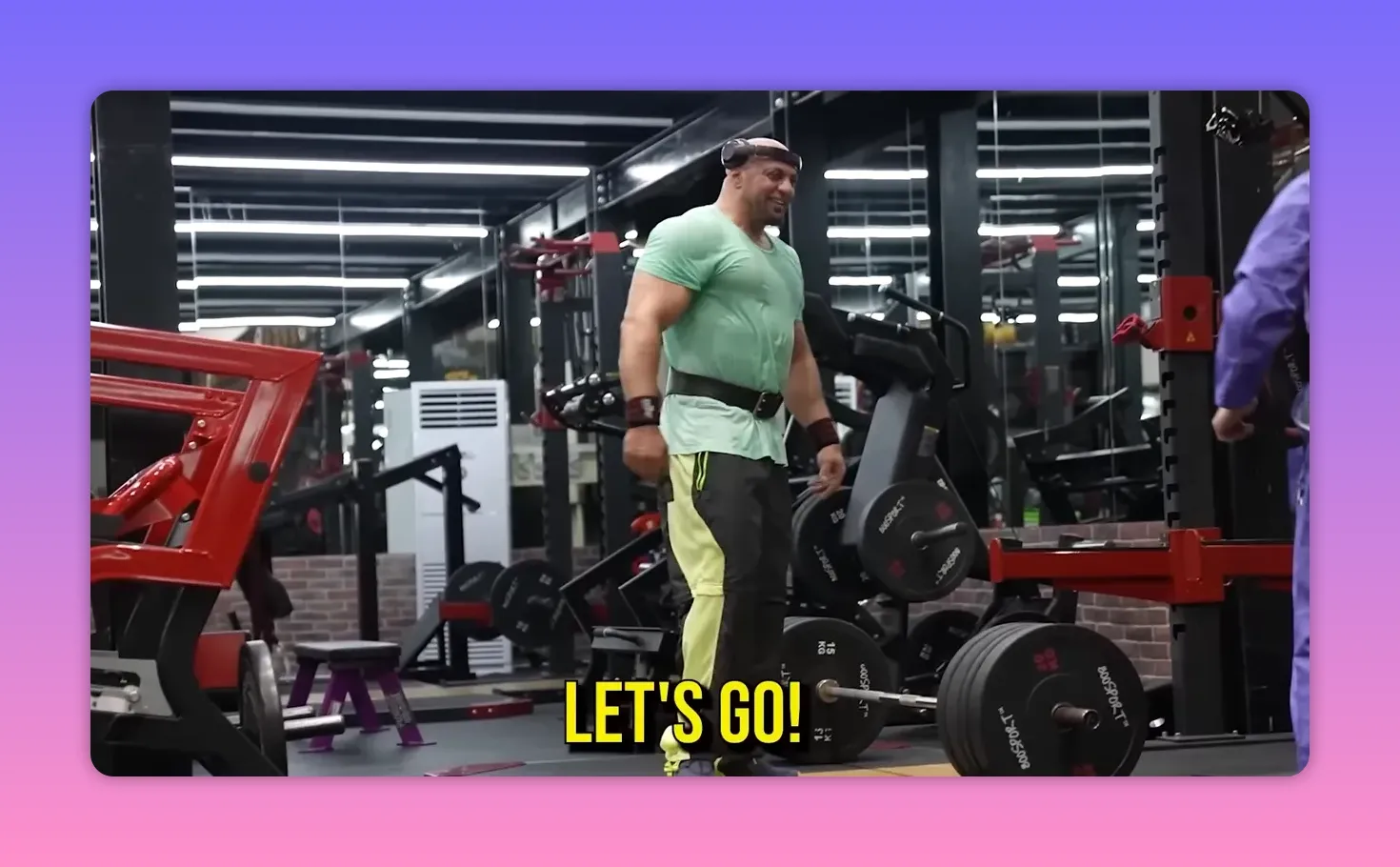 Muscular lifter in a green shirt standing beside a loaded barbell in a gym while a man in blue coveralls stands to the side, bold on-screen text reads 'LET'S GO!'